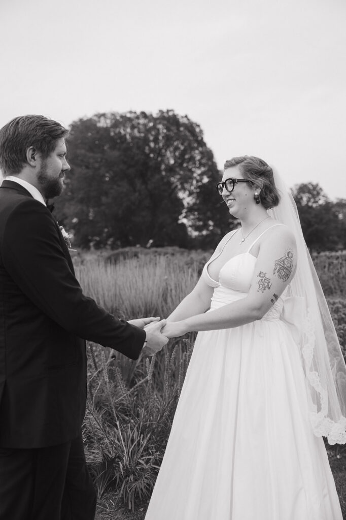 Black and white wedding portrait of a bride and groom holding hands and smiling at each other.