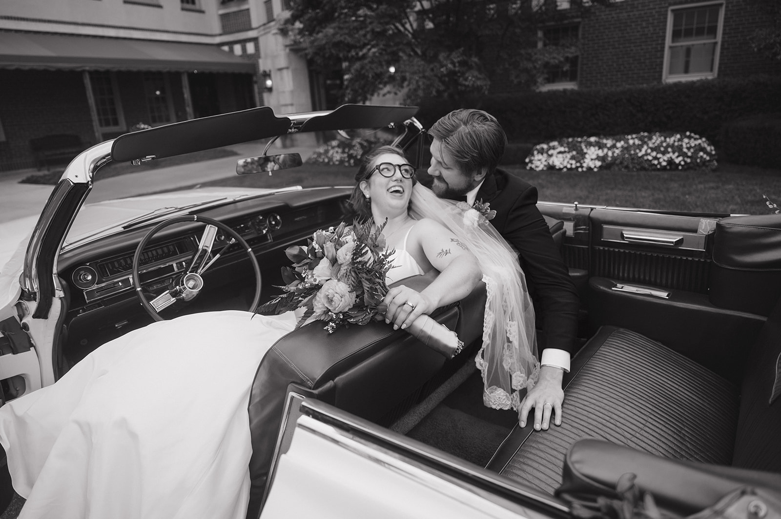 Black and white portrait of a bride and groom smiling at each other in a vintage Eldorado outside of Detroit Yacht Club.