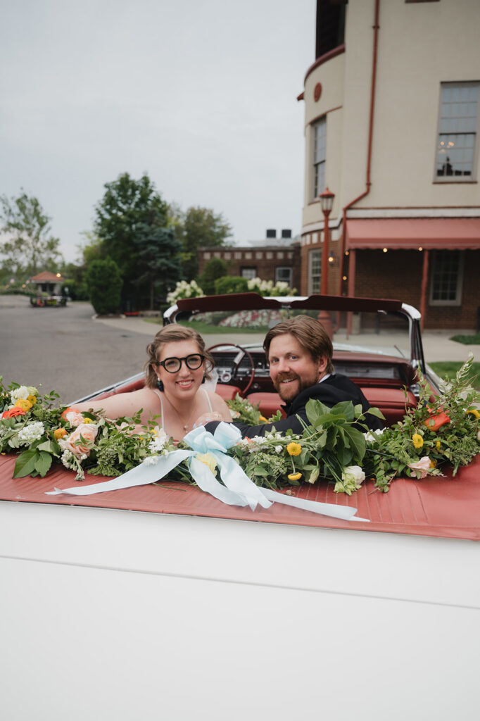 Bride and groom smiling at the camera while posing in a vintage Eldorado outside of Detroit Yacht Club.