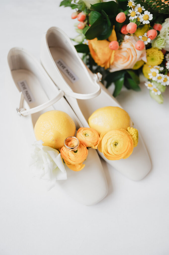 Brides shoes and colorful summer bouquet with lemons and rings.