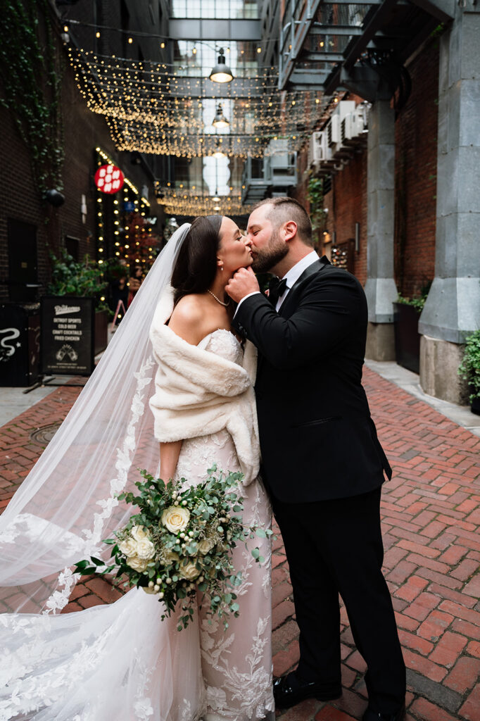 Bride and groom kissing in The Belt alley in downtown Detroit under string lights.