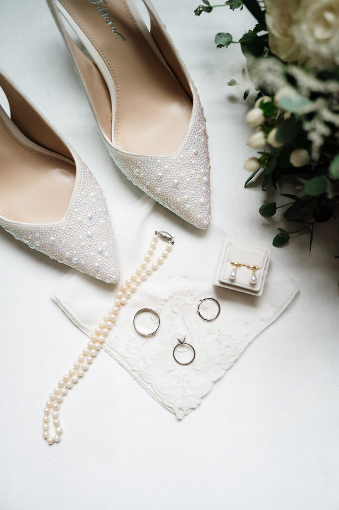 Brides wedding details with heels, rings, pearls, and other jewelry.