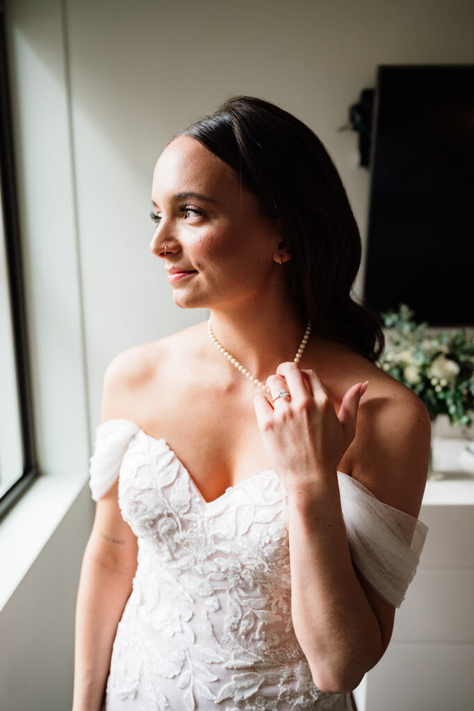 Bride looking out the window in her wedding dress with soft natural light at Element by Westin Detroit.