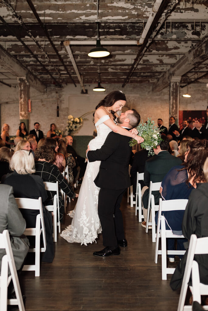 Groom lifting bride during ceremony exit at Ford Piquette Avenue Plant wedding.