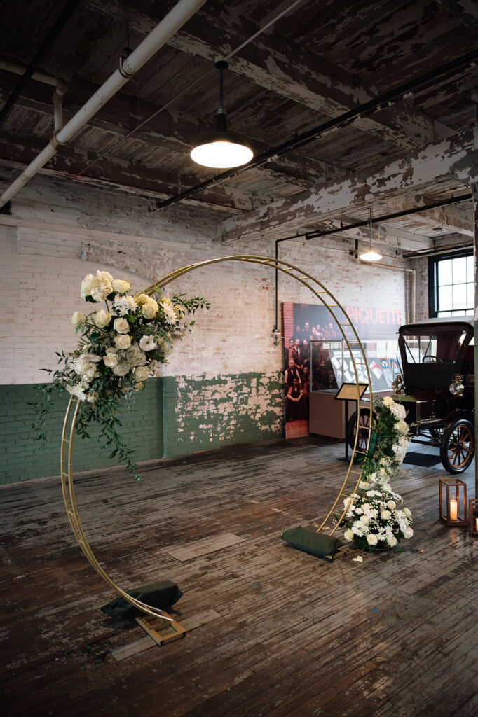 Floral ceremony arch with white and green arrangements inside Ford Piquette Avenue Plant wedding.