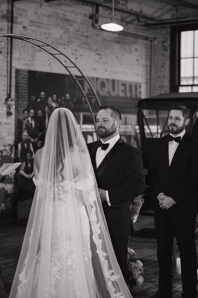 Black and white portrait of a bride and groom holding hands at the altar for their Ford Piquette Avenue Plant wedding ceremony in Detroit. 