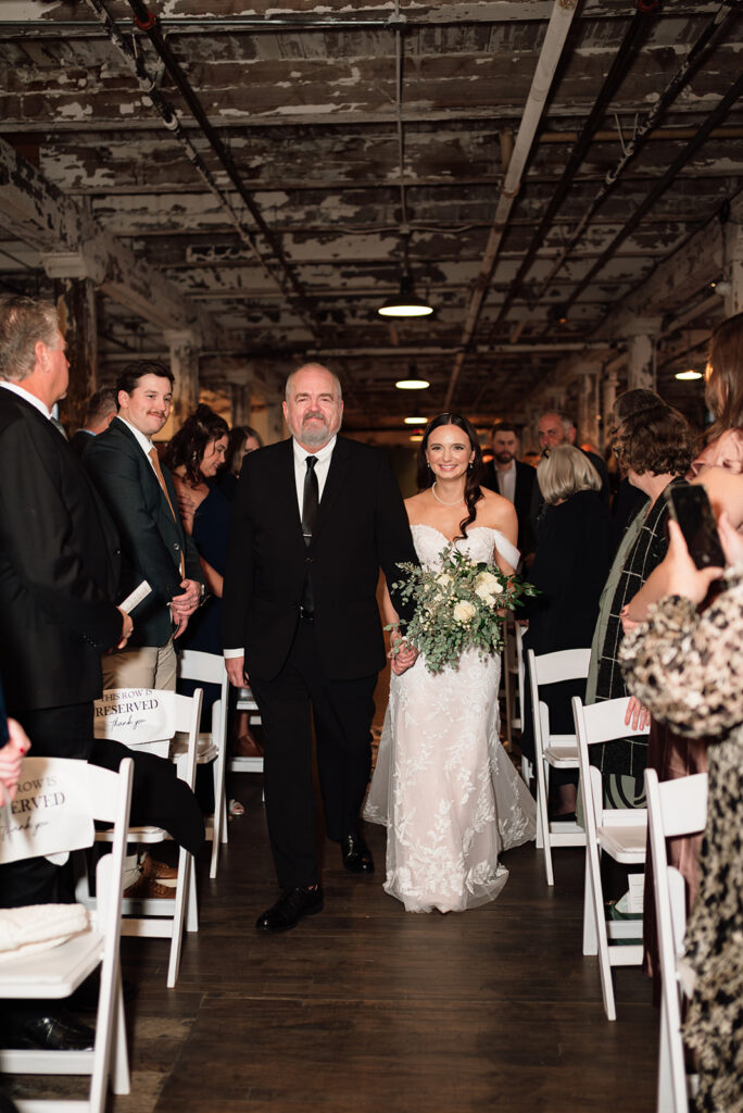 Bride walking down the aisle with her dad during Ford Piquette Avenue Plant wedding ceremony.