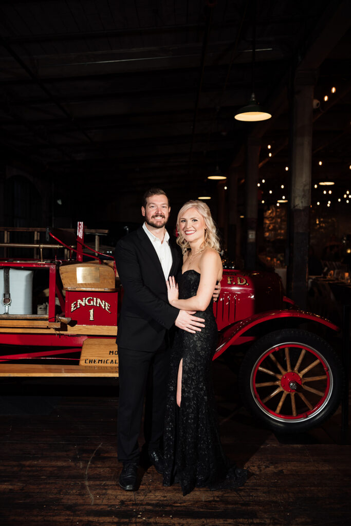 Guest couple smiling for portrait in front of vintage car at Ford Piquette Avenue Plant.