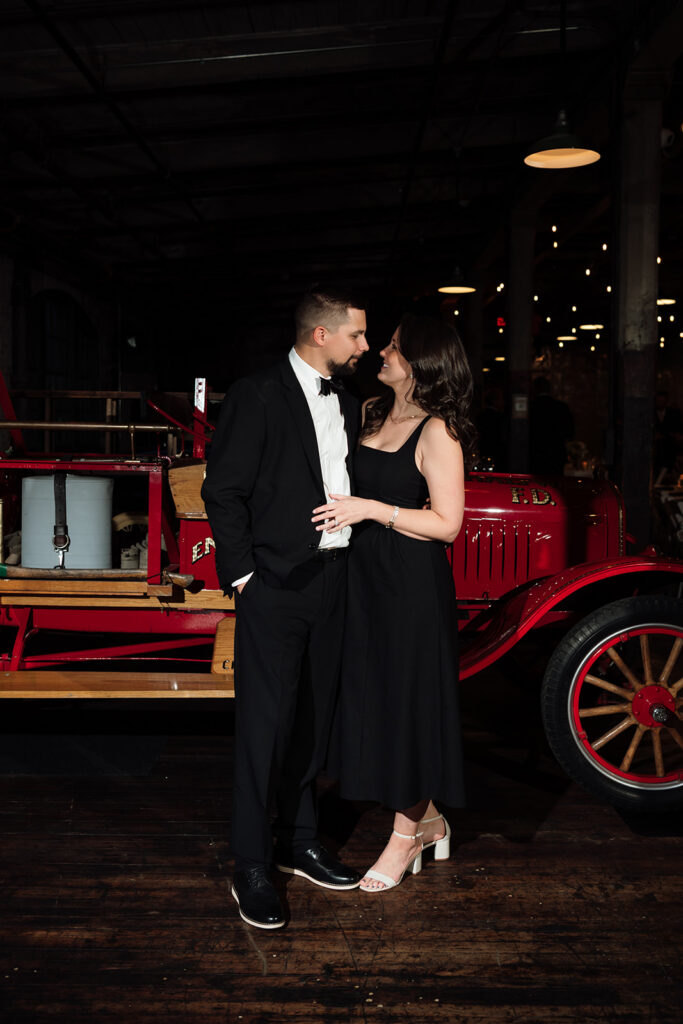 Guest couple smiling for portrait in front of vintage car at Ford Piquette Avenue Plant.