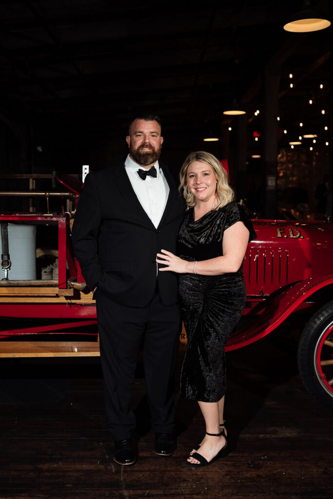 Guest couple smiling for portrait in front of vintage car at Ford Piquette Avenue Plant.