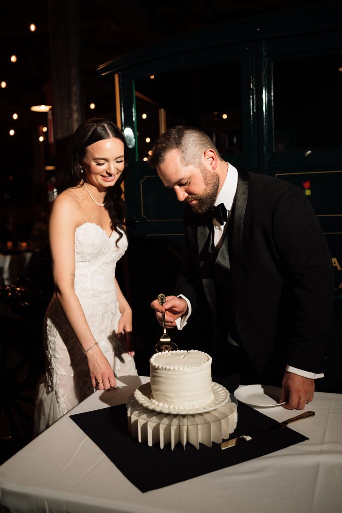 Bride and groom cutting into their cake during reception under string lights at Ford Piquette Avenue Plant.