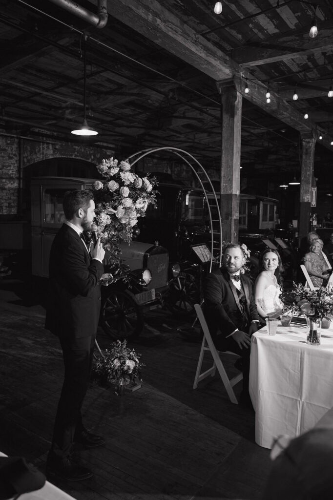 Black and white portrait of a guest giving a speech during a Ford Piquette Avenue Plant wedding reception.