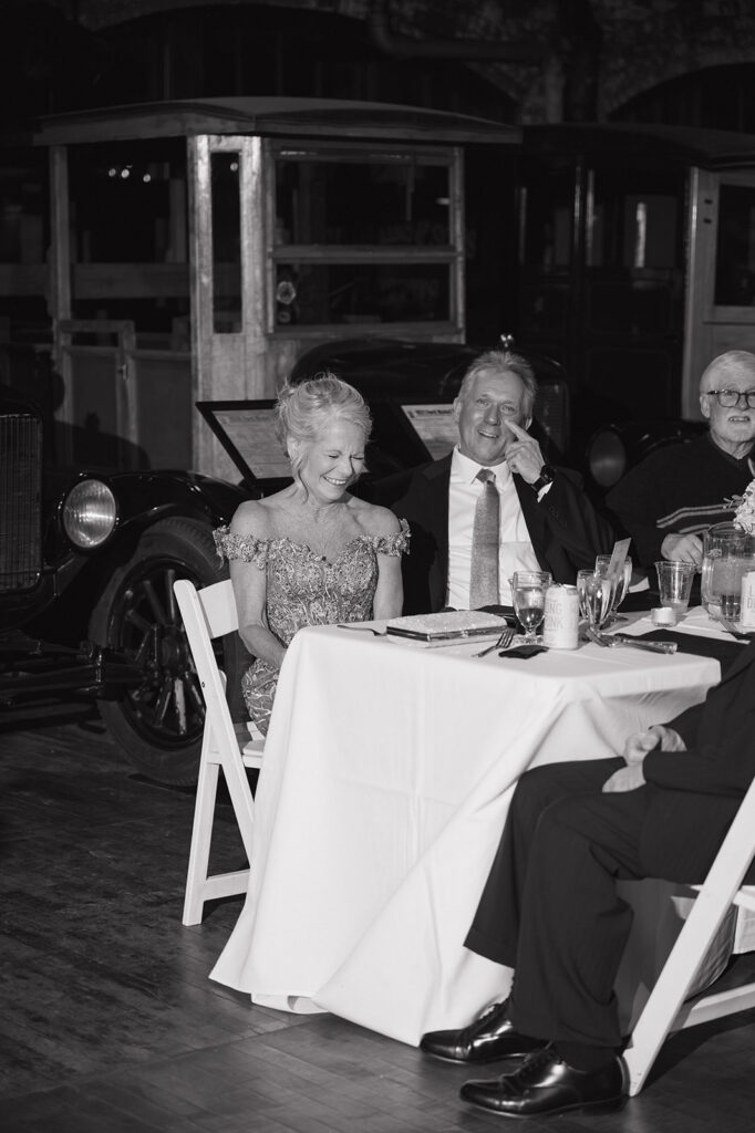 Black and white candid photo of guests laughing during reception speeches.