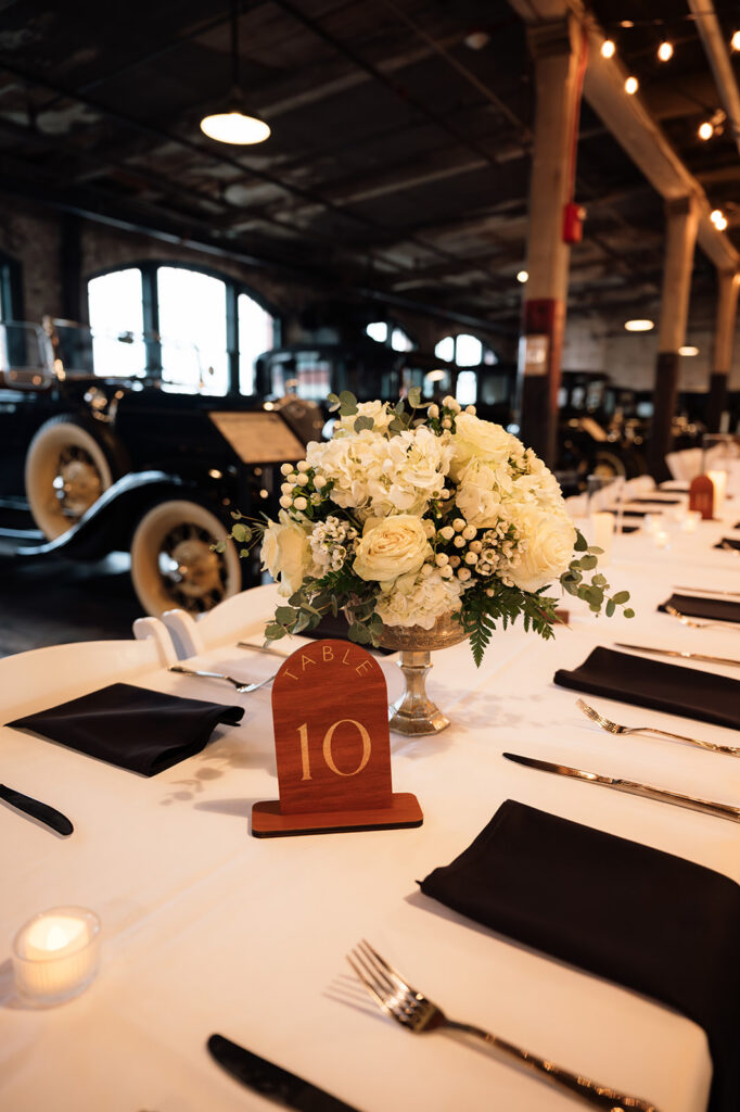 Floral centerpiece with white blooms and greenery on reception table at Ford Piquette Avenue Plant wedding.