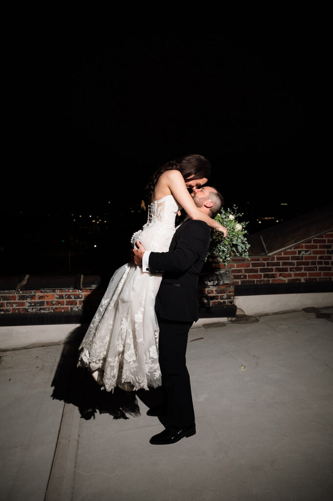 Bride and groom kissing on rooftop at night during wedding portraits.