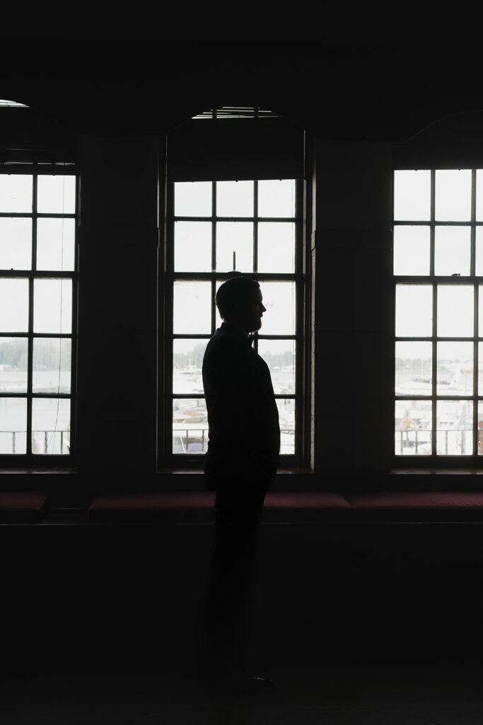 Dramatic indoor grooms portrait in front of the windows of Detroit Yacht Club.
