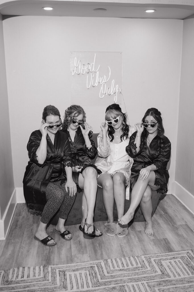 Black and white photo of a bride and bridesmaids sitting on a couch with sunglasses.