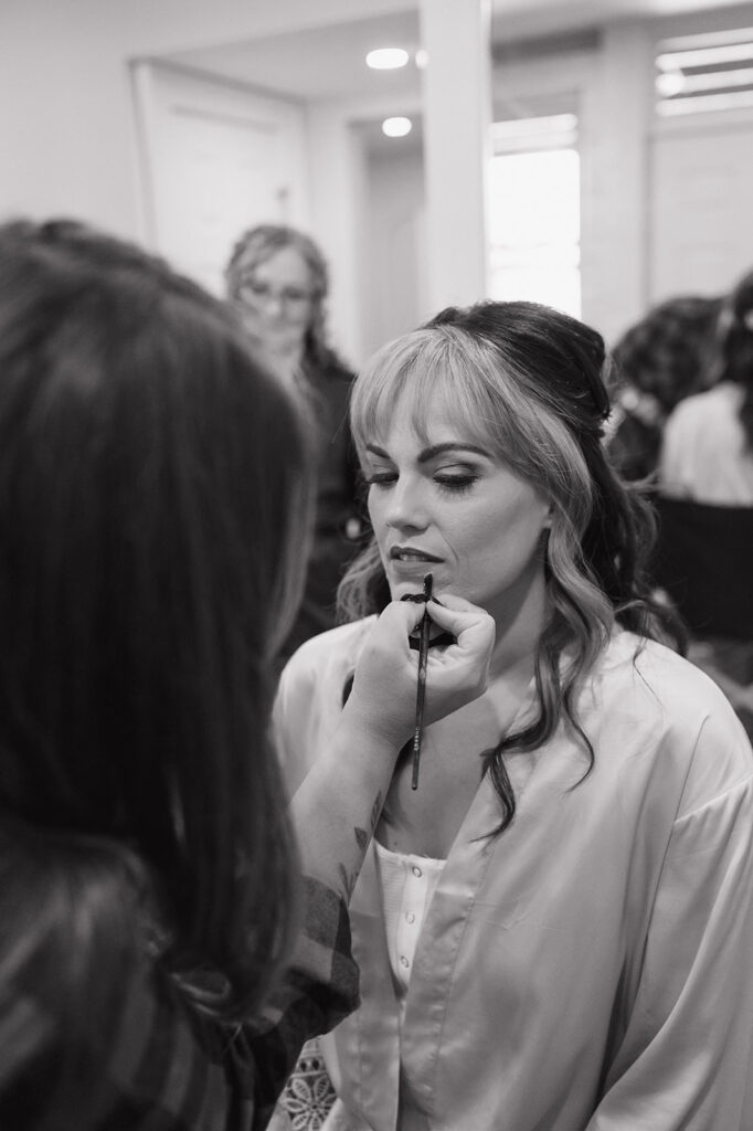Black and white photo of the bride getting her makeup done.
