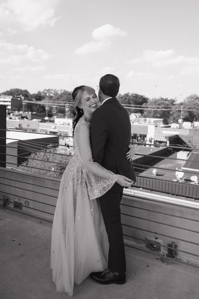 Bride and groom laughing on a rooftop during black and white wedding portraits.