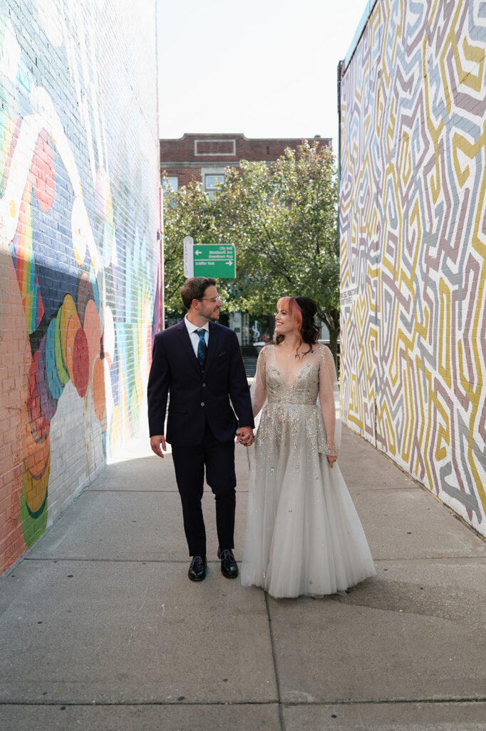 Bride and groom walking together between colorful murals during their Ferndale Michigan wedding.