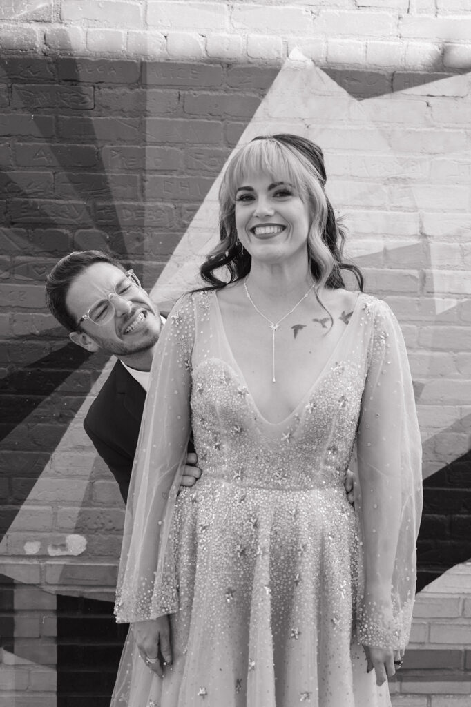 Bride and groom laughing together during black and white wedding portraits in Ferndale, Michigan.