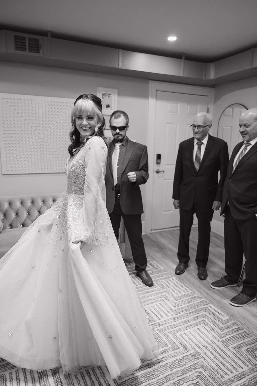 Black and white photo of a bride showing her family her wedding attire.