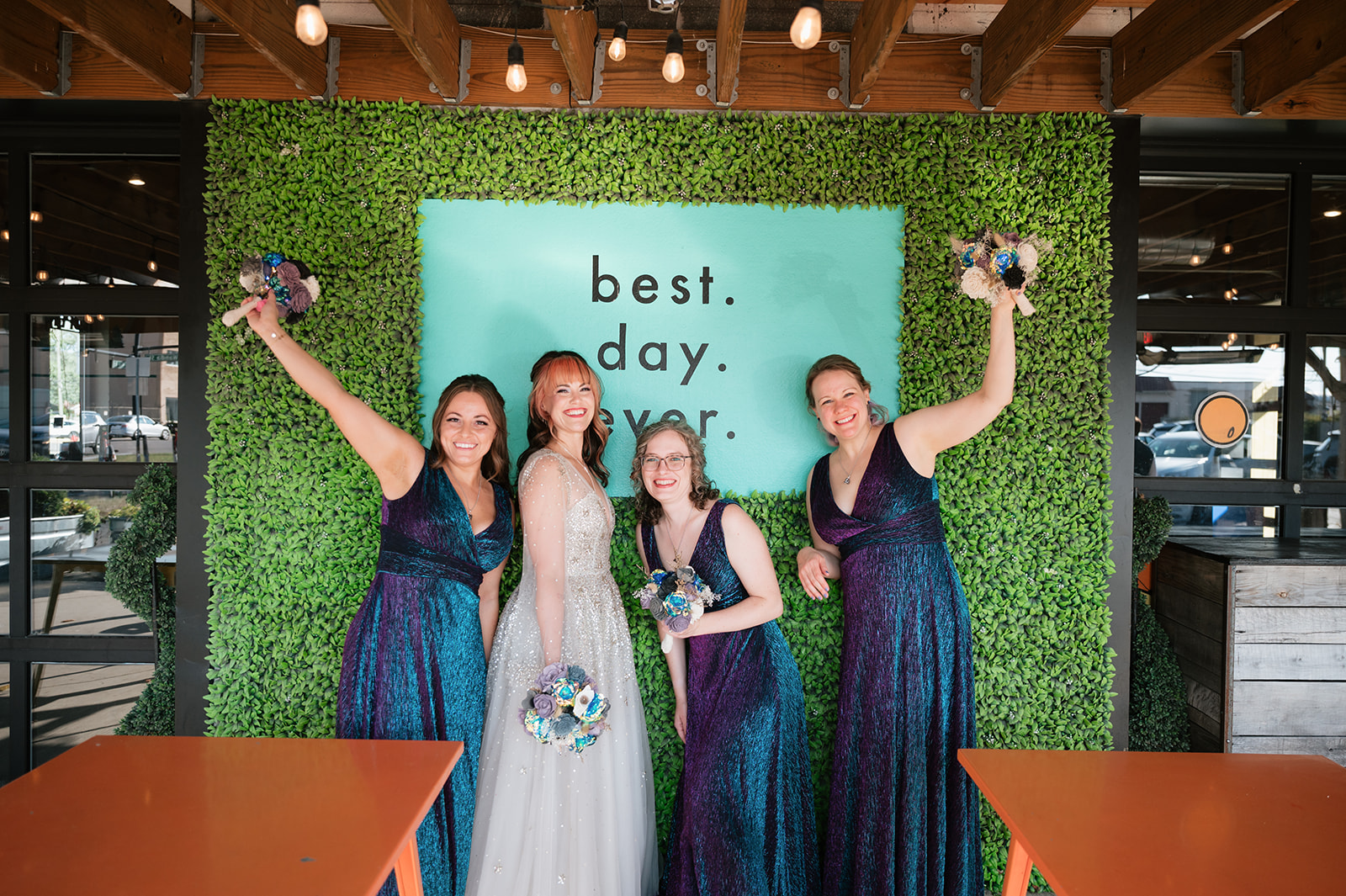 Bride and bridesmaids posing in front of a greenery wall at Detroit Fleat.