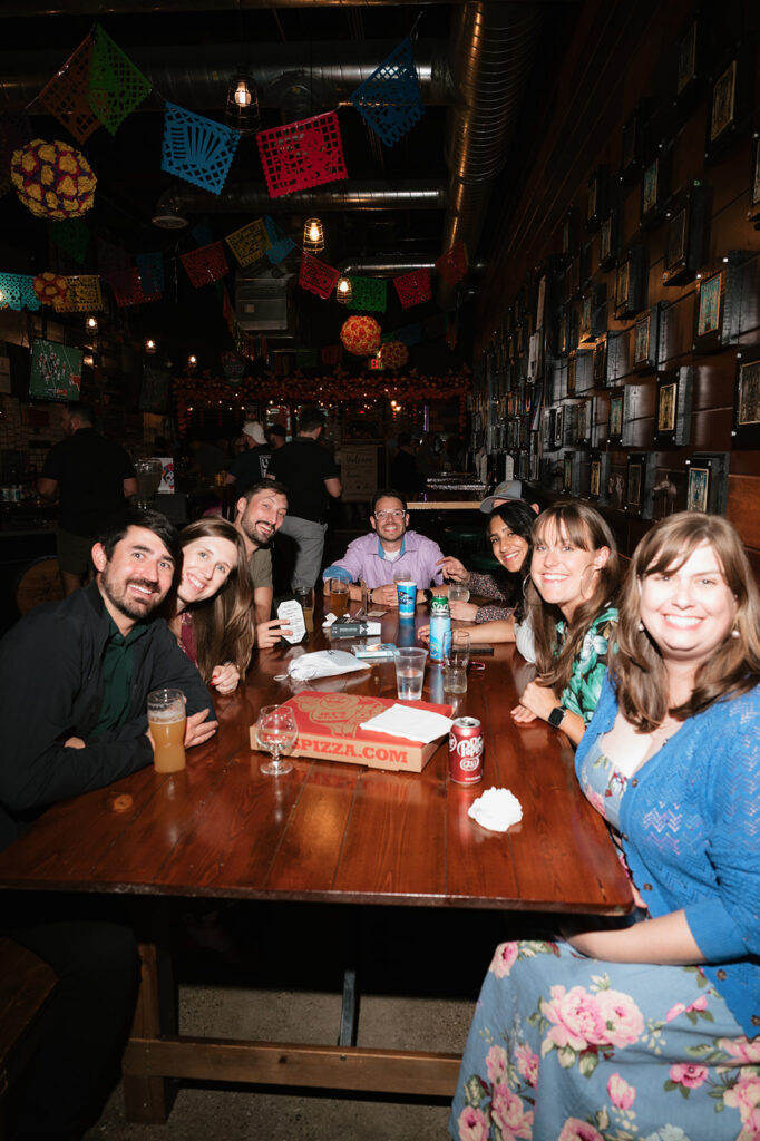 Guests gathered around a table with pizza and drinks during a relaxed rehearsal dinner.