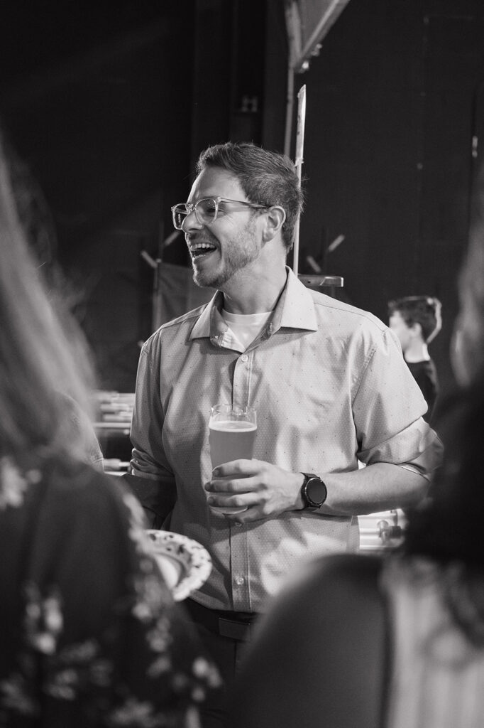 Groom laughing with a drink during a black and white rehearsal dinner photo.