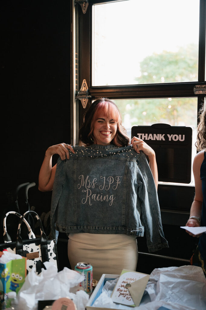 Bride smiling while holding a custom jacket during her rehearsal dinner at Dog and Pony Show Brewing.