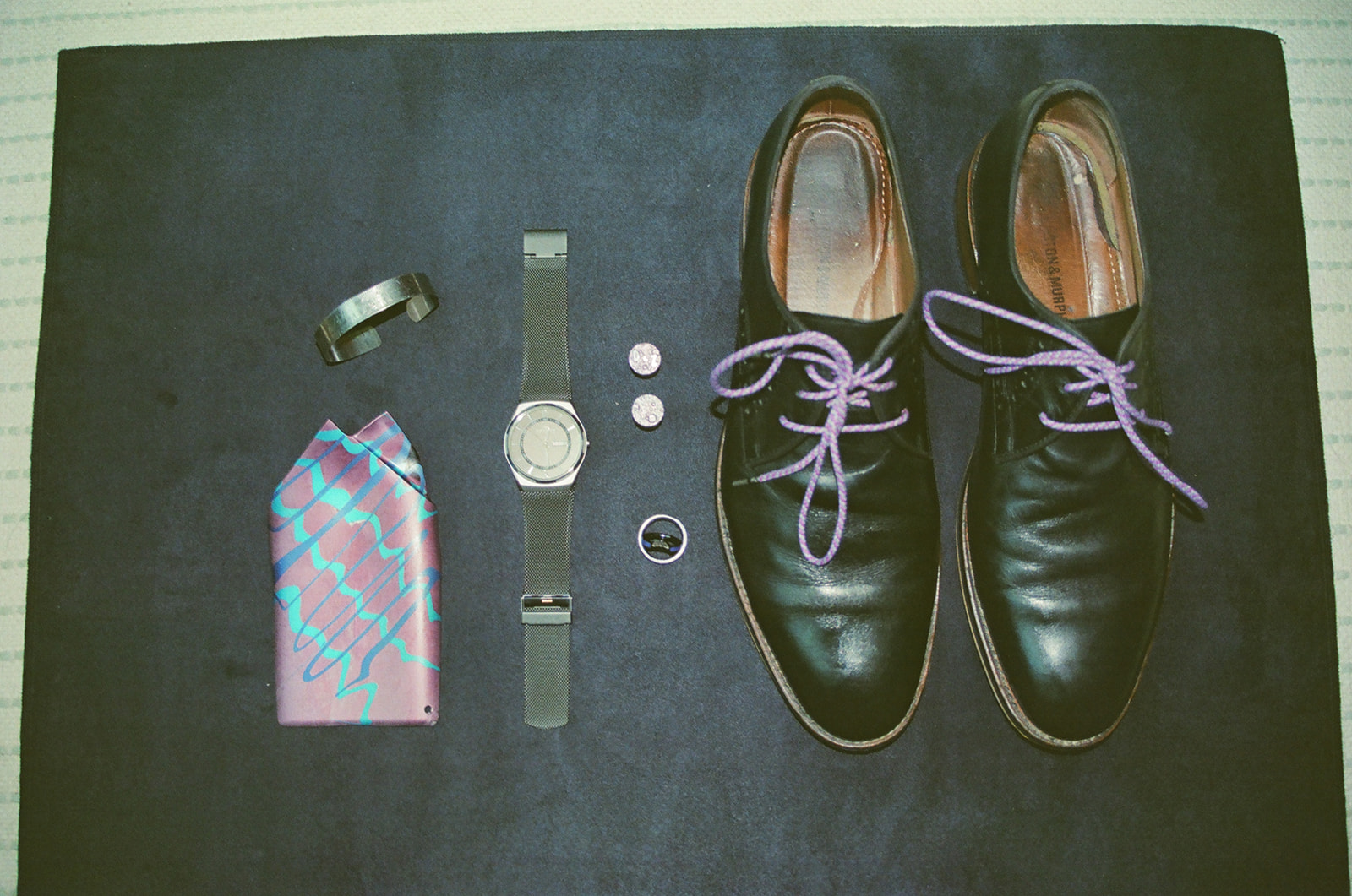 Groom’s wedding details photographed on film with black shoes, purple laces, watch, cufflinks, and pocket square.