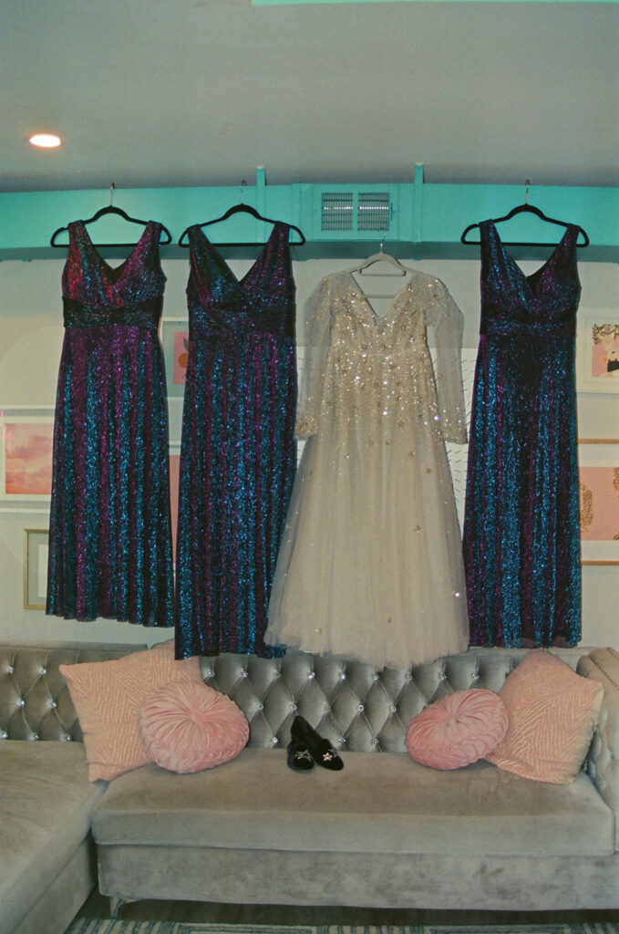 Bride and bridesmaid dresses hanging above a couch on film before a Ferndale Michigan wedding.