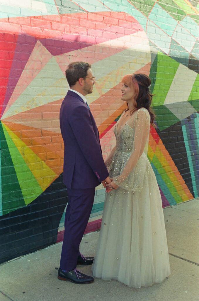 Bride and groom holding hands in front of a colorful mural during their Ferndale Michigan wedding on film.