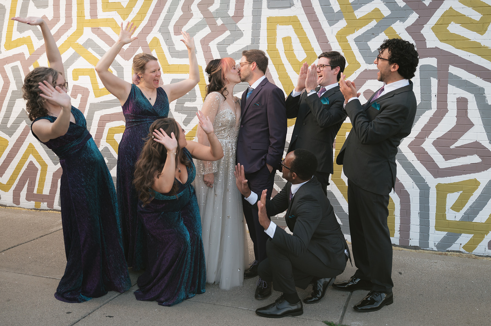 Bride and groom kissing while their wedding party laughs during portraits in Ferndale, Michigan.