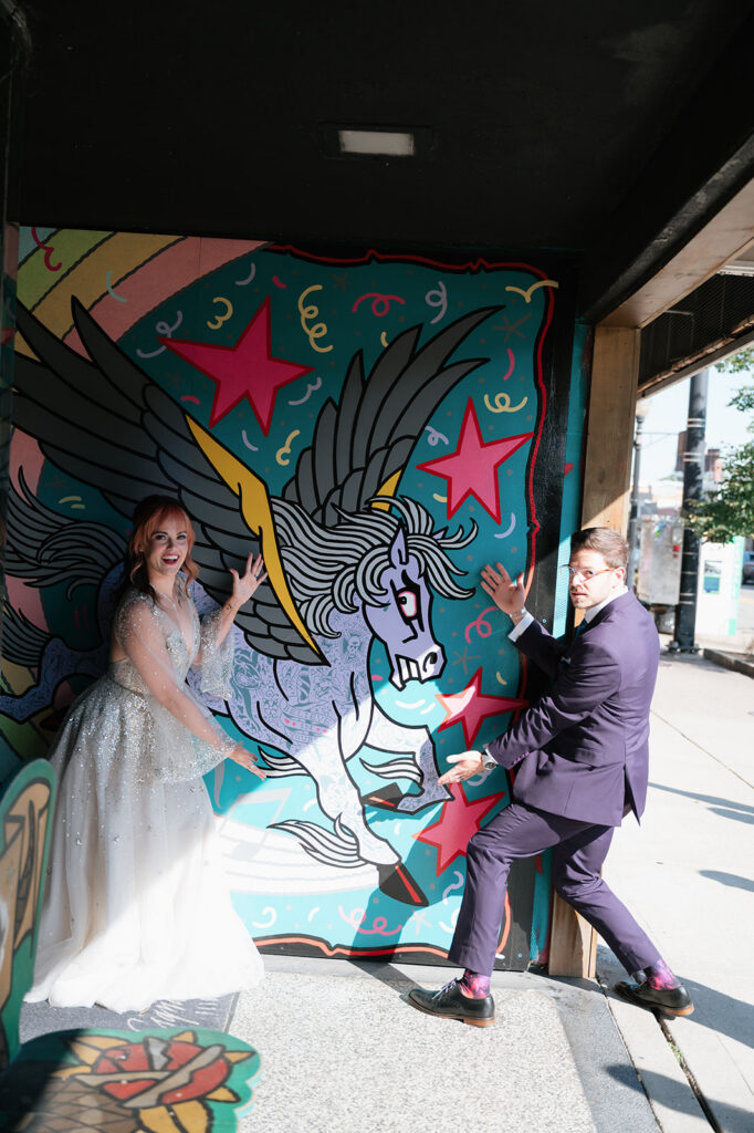 Bride and groom posing playfully in front of a unicorn mural during their Ferndale Michigan wedding.