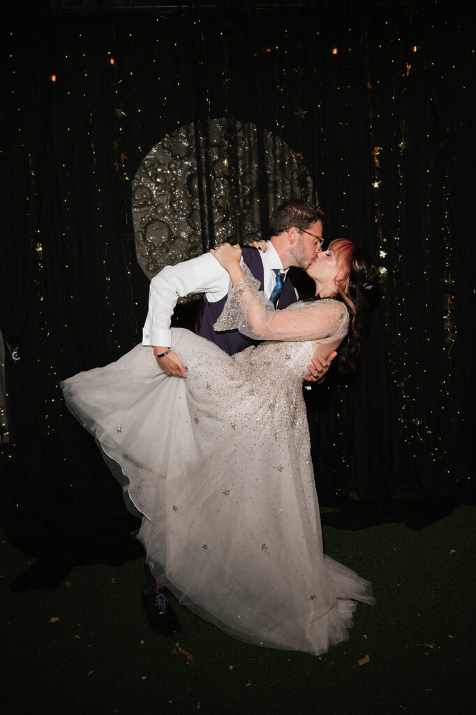 Bride and groom kissing in front of their moon wedding backdrop.