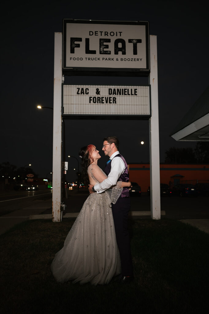 Bride and groom posing under the Detroit Fleat sign that reads Zac & Danielle Forever.