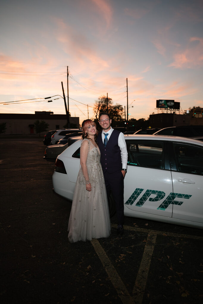 Bride and groom posing in front of the grooms work car.