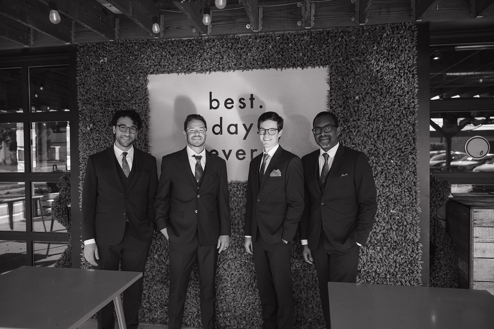 Black and white photo of the groom and his groomsmen in front of a greenery wall at Detroit Fleat.
