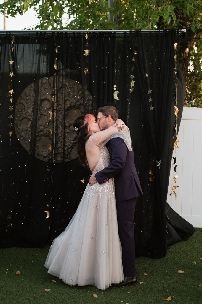 Bride and groom kissing in front of a handmade moon backdrop during their Detroit Fleat wedding.