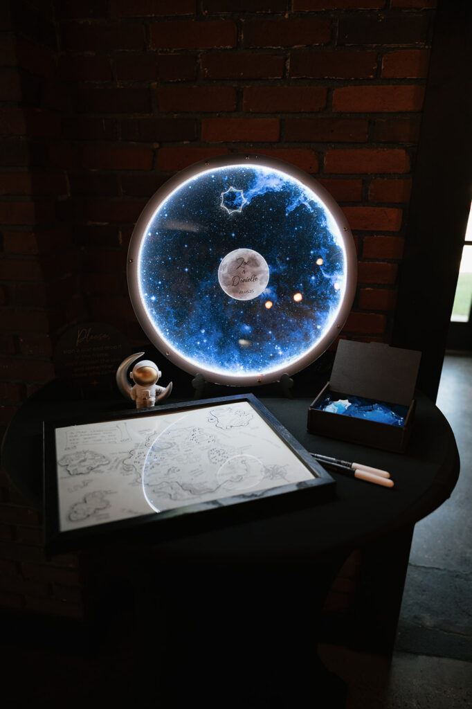 Space-themed guest book table with a light-up moon sign and hand-drawn map for a Ferndale Michigan wedding.