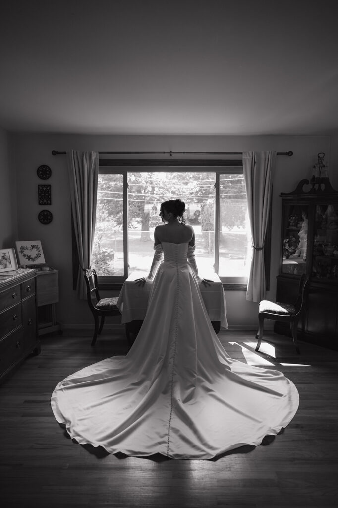 Bride standing by a window in her wedding dress during black and white getting ready portraits.