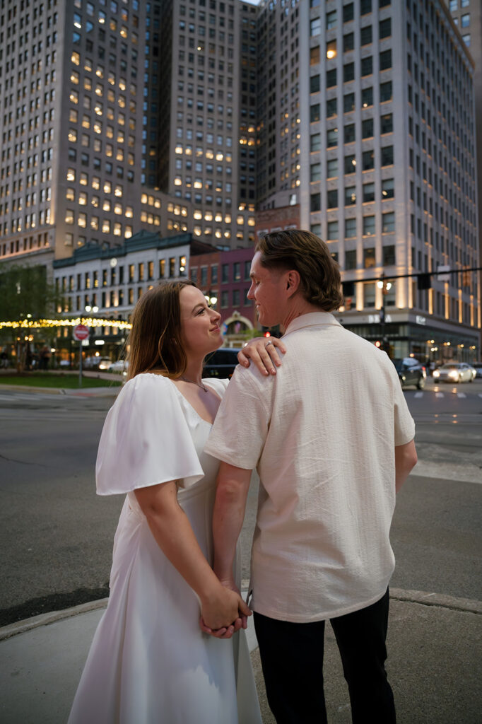 Couple smiling together downtown with the city lights on behind them.