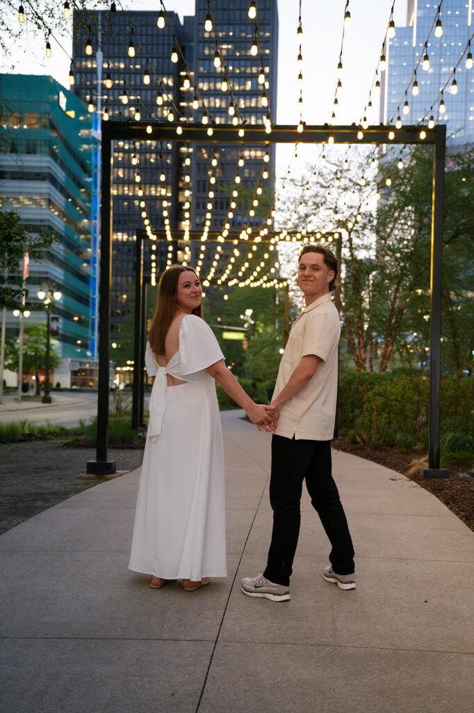 Couple walking beneath string lights in downtown Detroit as the city lights turn on.