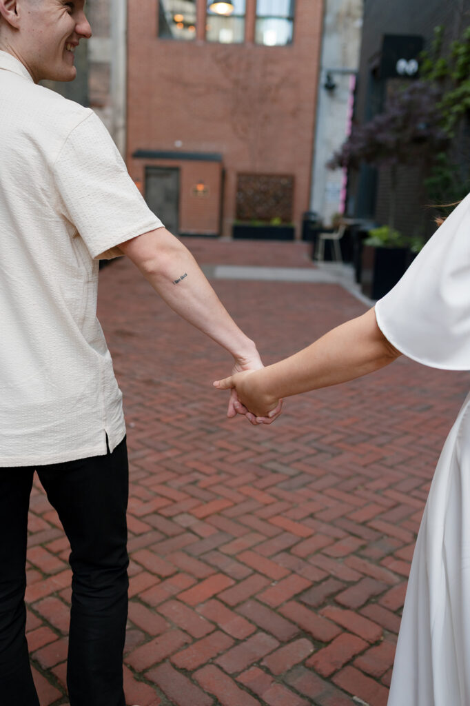 Couple holding hands and walking together in The Belt during their downtown Detroit engagement photos.