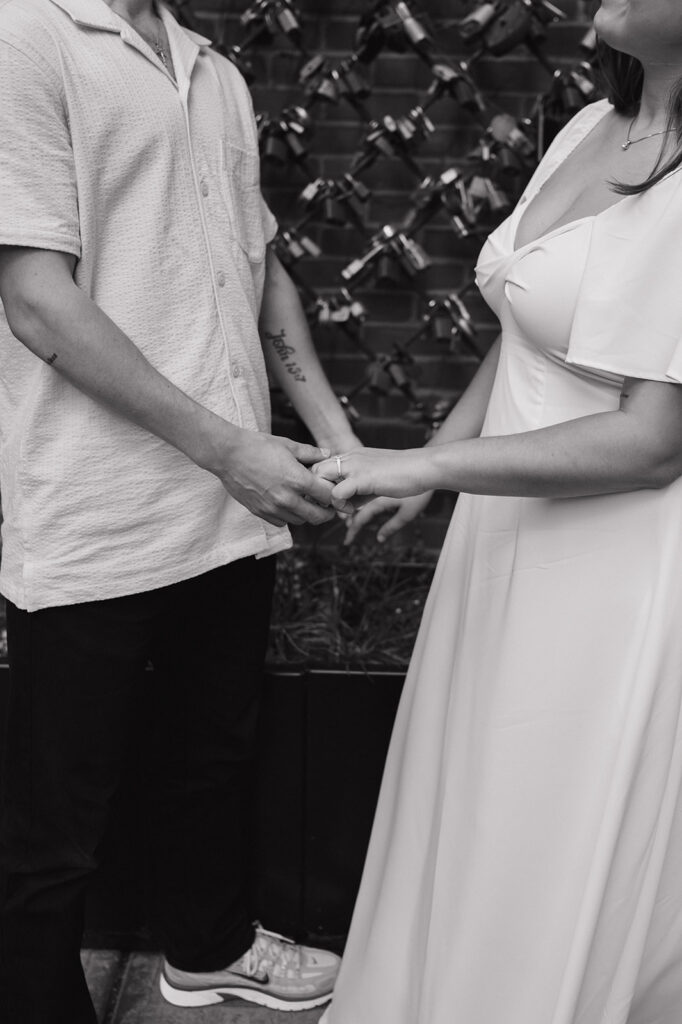 Couple holding hands in front of a brick wall and lock installation in The Belt.