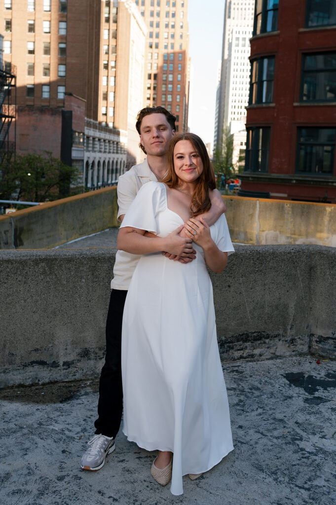 Couple posing on a rooftop for their Detroit engagement photos with the skyline behind them.