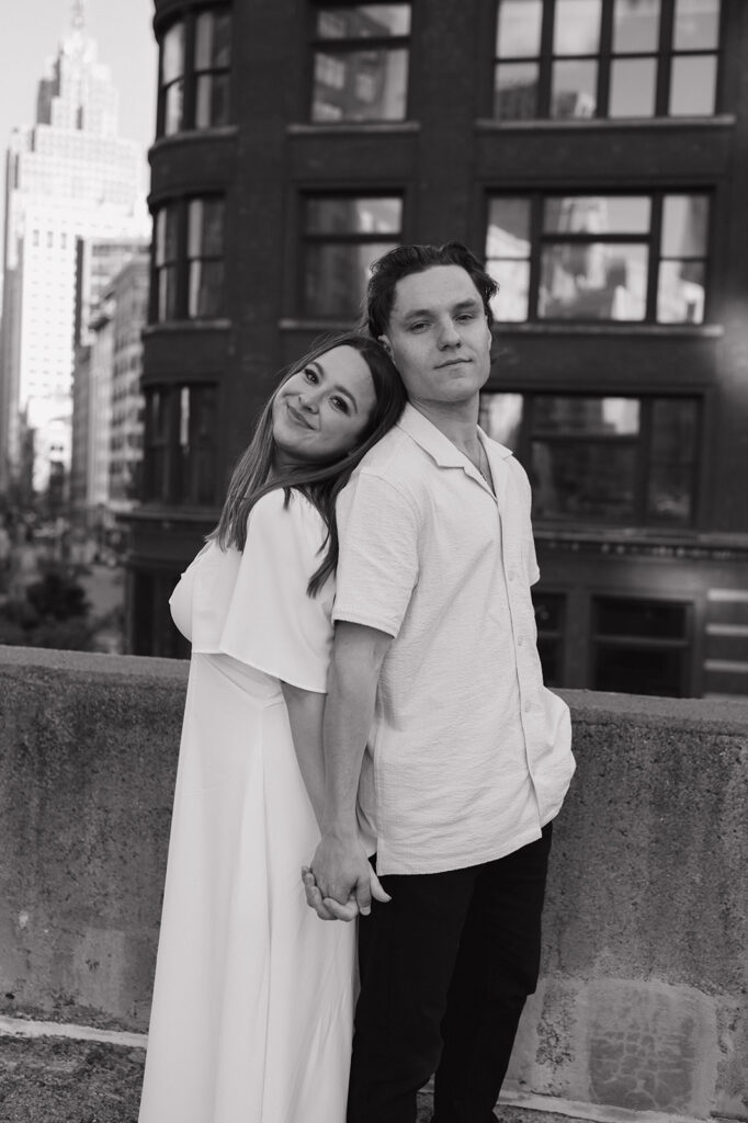 Black and white photo of a couple standing back to back on a rooftop for their Detroit engagement photos.