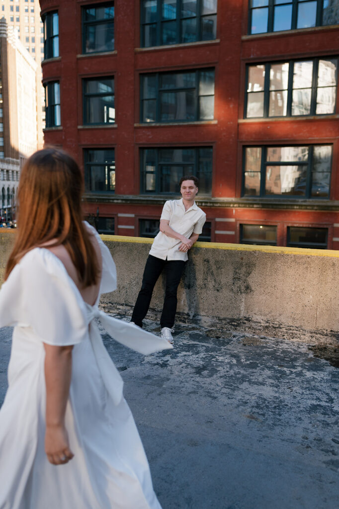 Editorial style photo of a man watching his fiancé walk on a rooftop. 
