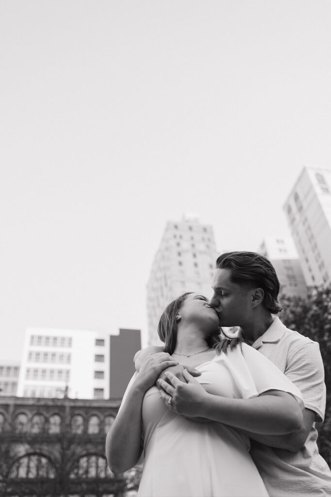 Photo from below of  couple kissing with the Detroit skyline above them. 